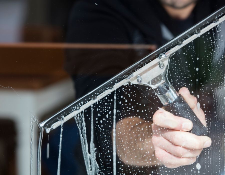 Professional window cleaning service by Bullseye Cleaning in the Lowcountry, featuring a close-up of a technician using a squeegee to remove soap and grime for streak-free, crystal-clear glass results