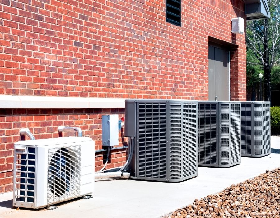 "Outdoor view of commercial HVAC systems and residential mini-split unit installed by Coastal Heating and Air in the Lowcountry, lined up against a red brick wall for efficient climate control and ventilation