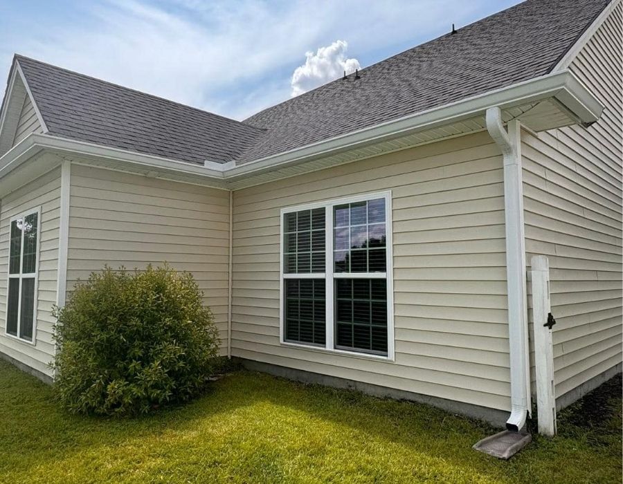 Lowcountry home with beige vinyl siding, white double-pane windows, and professionally installed seamless white gutters and downspouts by Gutter Xperts, showcasing clean exterior drainage solutions and curb appeal