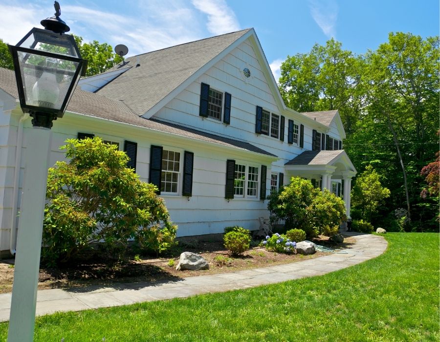 Classic two-story Lowcountry home with white wood siding, black shutters, and a neatly manicured lawn, framed by mature landscaping and a curved stone walkway leading to the front entrance