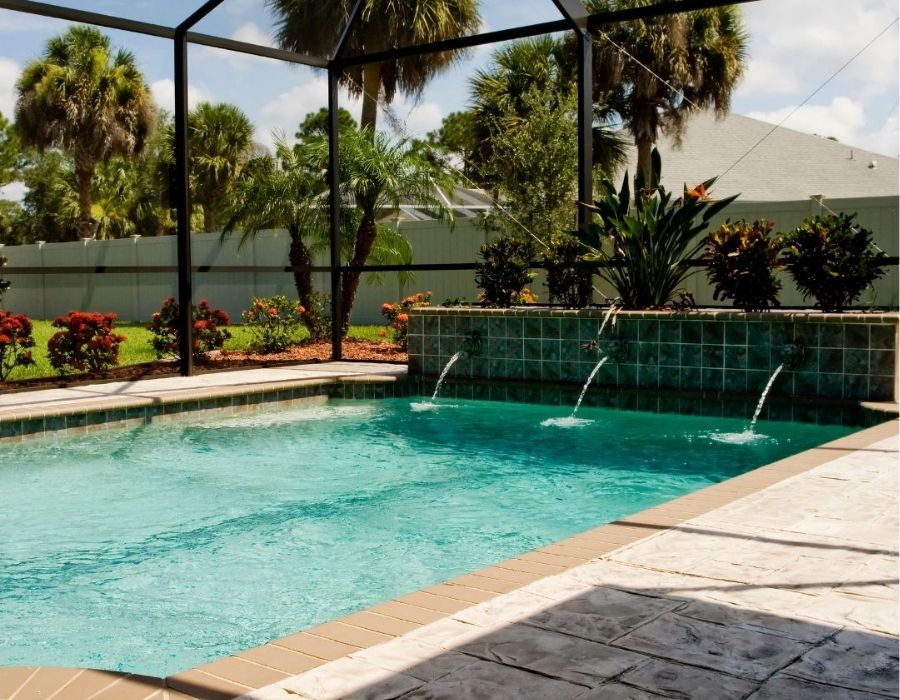 Custom backyard swimming pool with tile water features and screened enclosure by Pristine Pool Builders in the Lowcountry, surrounded by tropical landscaping and a stamped concrete patio for luxury outdoor living
