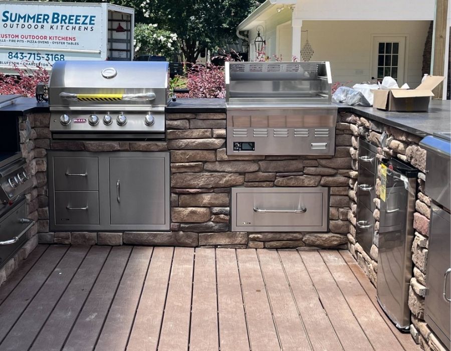 Custom stone outdoor kitchen setup by Summer Breeze Outdoor Kitchens in the Lowcountry, featuring built-in stainless steel grills, refrigeration drawers, and storage cabinets for a high-end backyard cooking experience