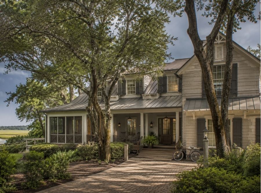 Luxury older Hilton Head Island vacation home in Sea Pines near marshland, classic Lowcountry architecture with screened porch and live oak trees, bicycles leaning near entryway, warm humid coastal atmosphere, subtle signs of summer storm season approaching, upscale second-home aesthetic, Palmetto Dunes and Shipyard style homes, soft marsh light
